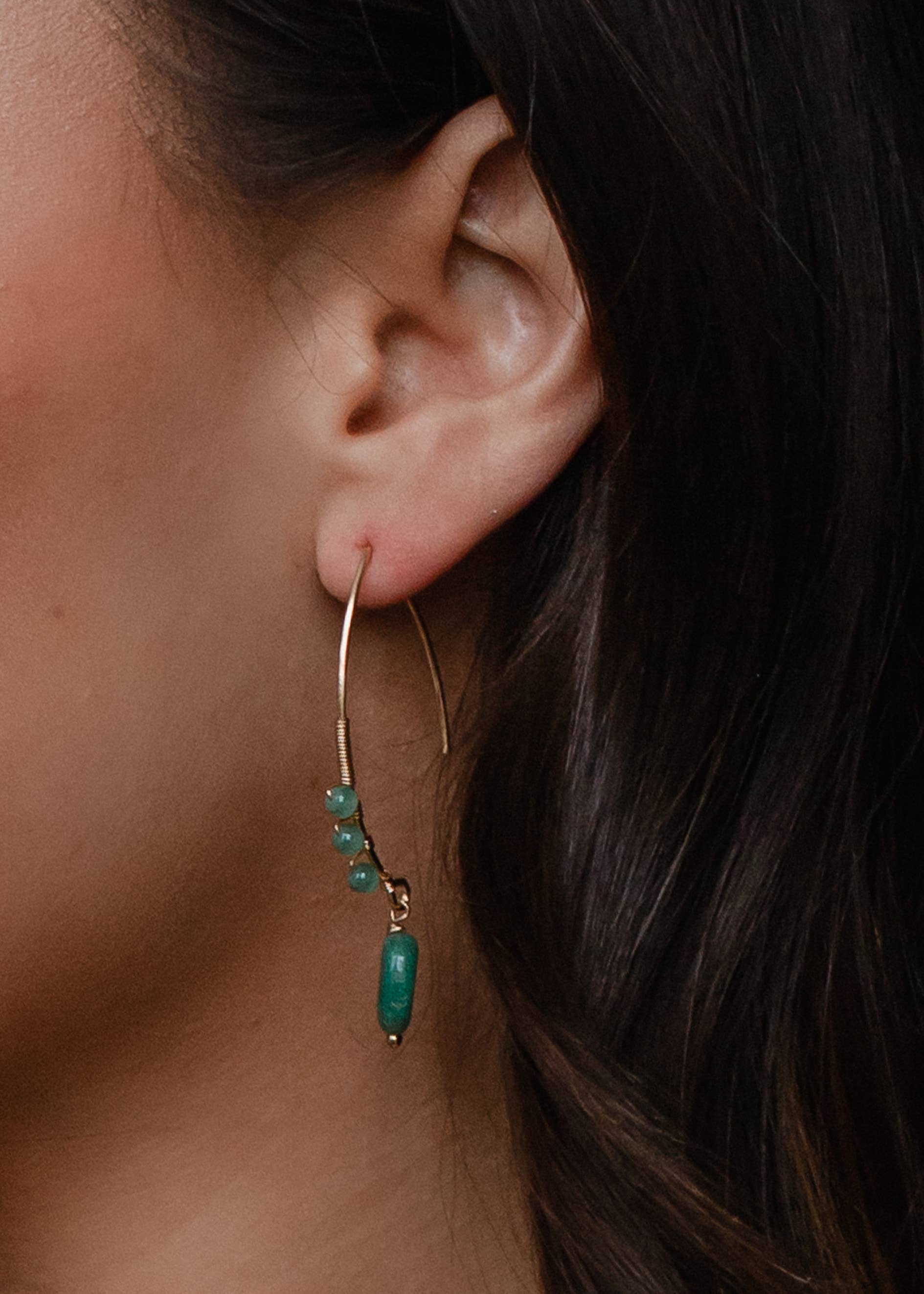 Close-up of a woman's ear wearing 2-inch gold detail beaded dangles earrings with green beads, lead and nickel free
