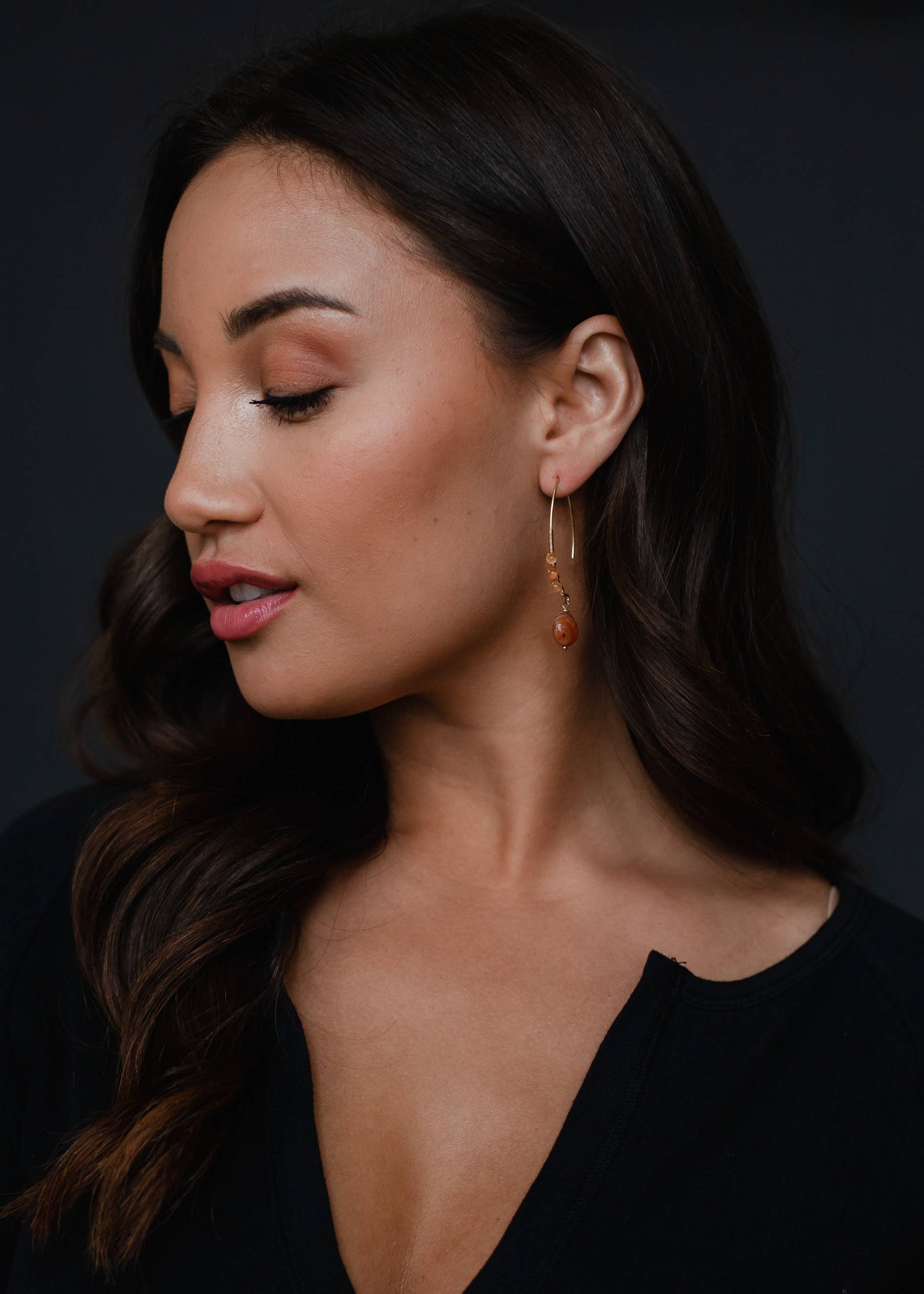 Woman wearing 2-inch gold detailed beaded dangles earrings, lead and nickel free, on dark background