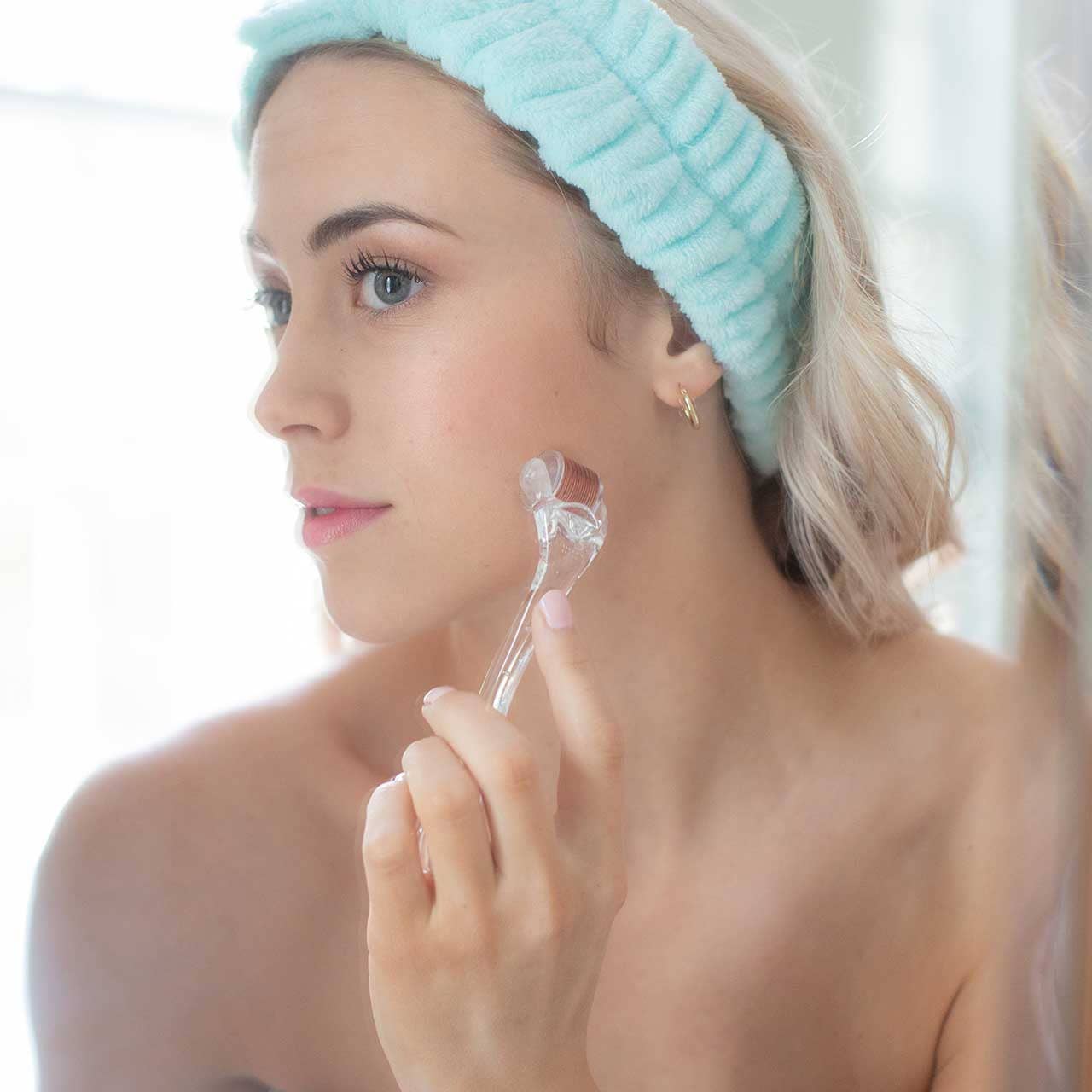 Woman using All About the Face Microneedle roller for skin renewal with blue headband