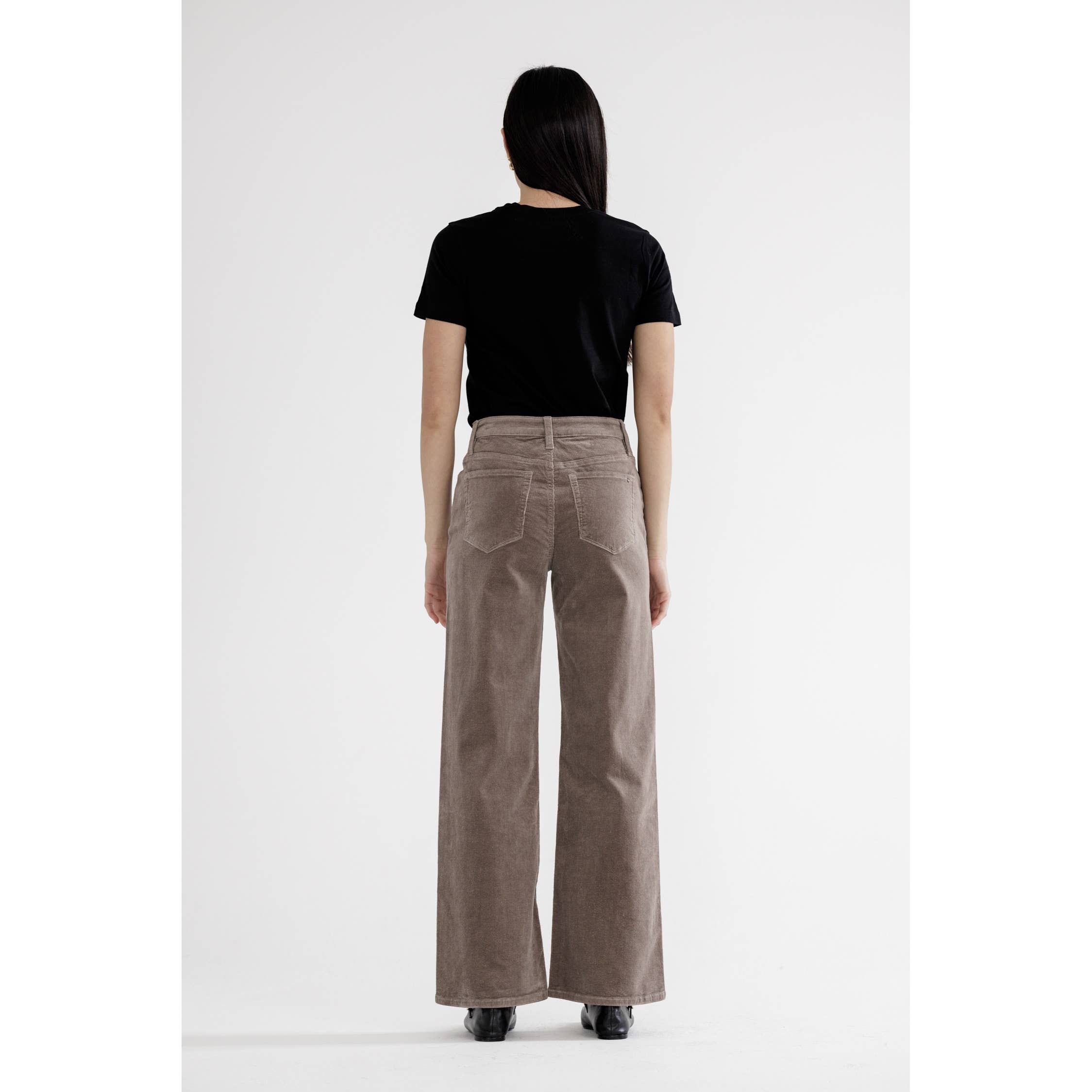 Woman wearing light greige high rise wide leg pants with black top, back view