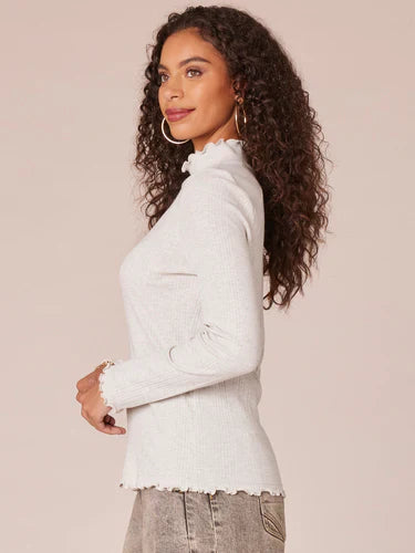 Woman wearing heather cream long raglan sleeve mock neck ribbed knit top with lettuce edge detailing