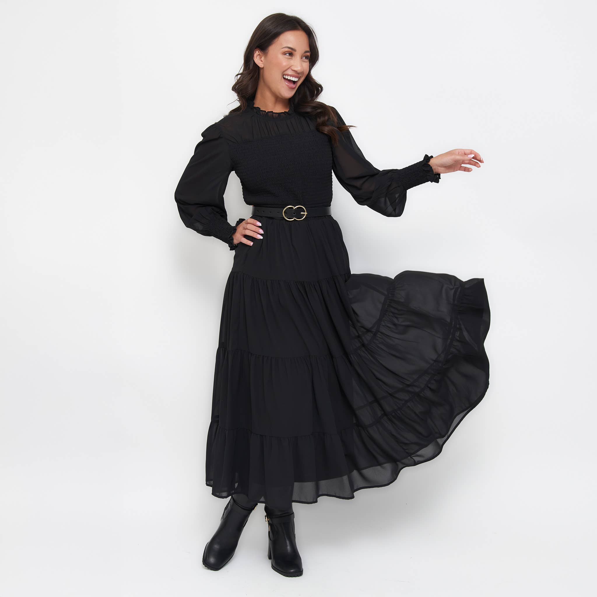 Woman wearing black Hazel Georgette Tiered Maxi Skirt with long sleeves and elastic waistband, twirling to show skirt's flowy tiers and side pockets.