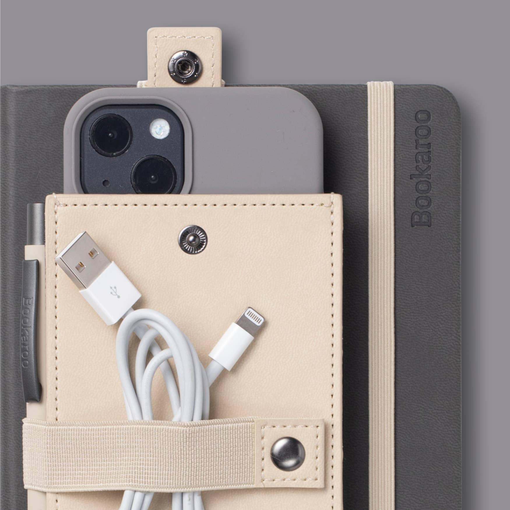 Bookaroo Phone Holder beige elastic strap holding phone charger on gray notebook with pen slot and snap button closure