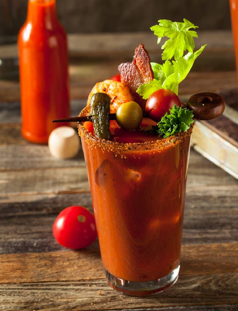 Bloody Mary cocktail in a glass with seasoned salt rim and garnished with celery, bacon, shrimp, olives, and cherry tomatoes